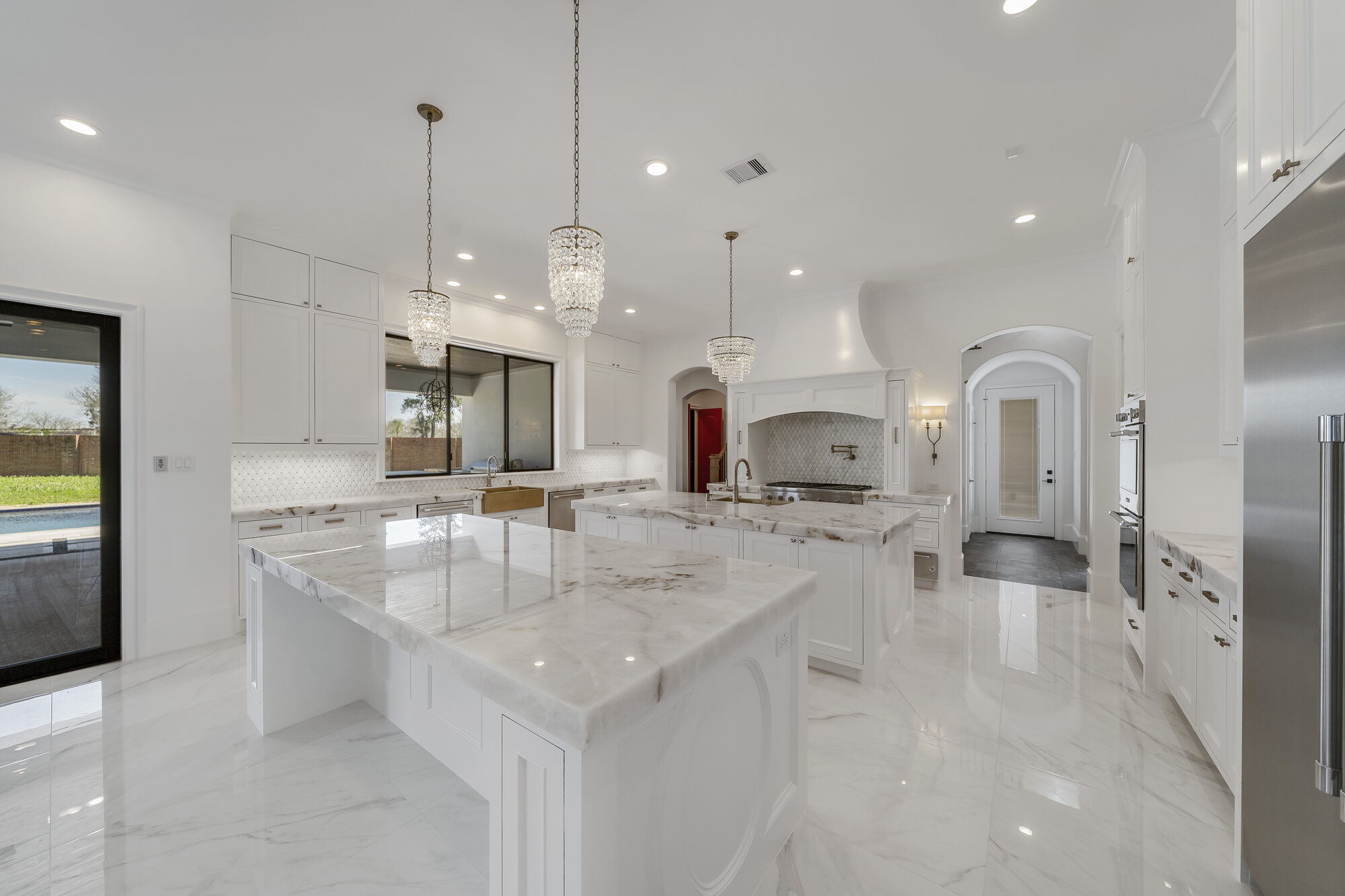 Psalms kitchen with twin marble islands, crystal pendants, and a professional range beneath a plaster hood