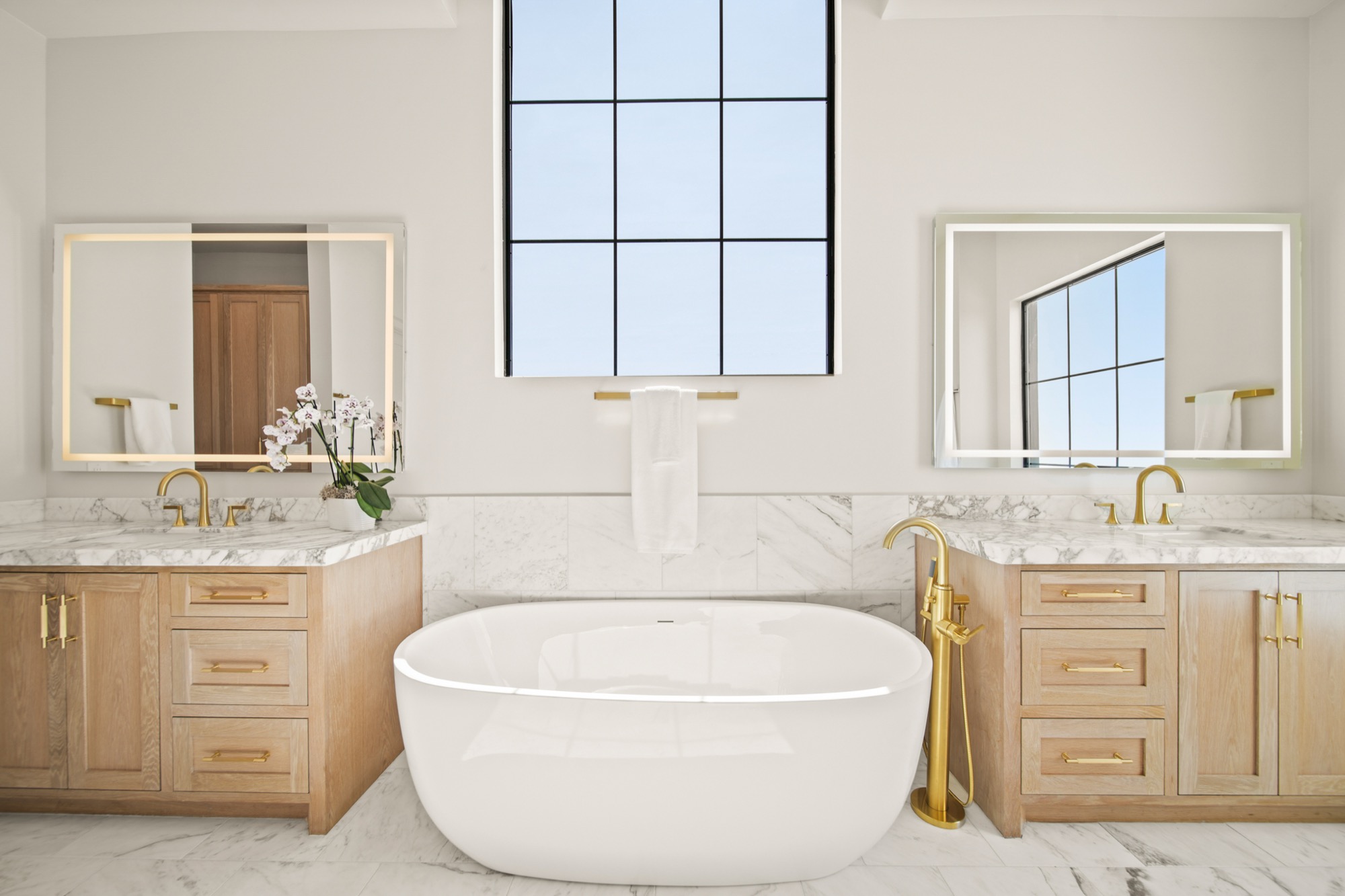 Primary bath with freestanding soaking tub, book-matched stone surrounds, and warm lighting